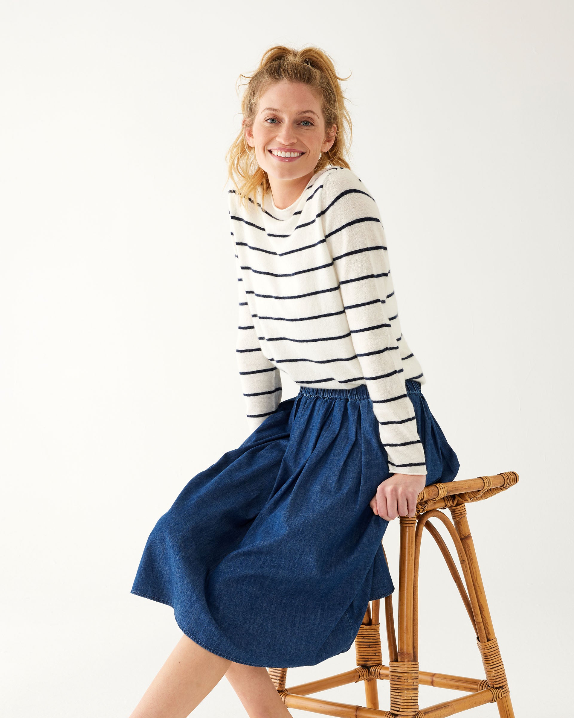 woman wearing Mersea carmel cashmere sweater in navy stripes sitting on stool leaning forward
