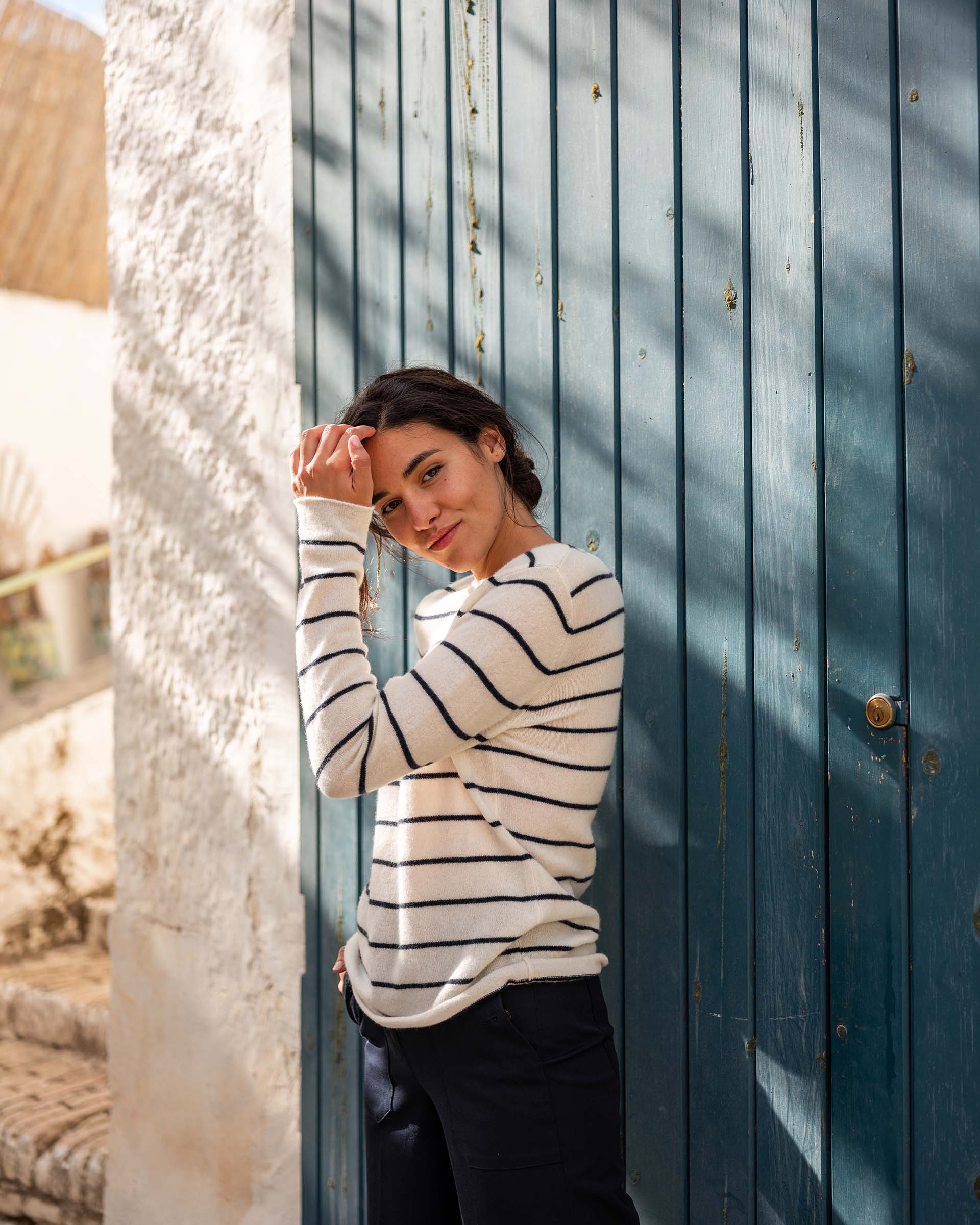 woman wearing Mersea carmel cashmere sweater in navy stripes standing in front of wooden door