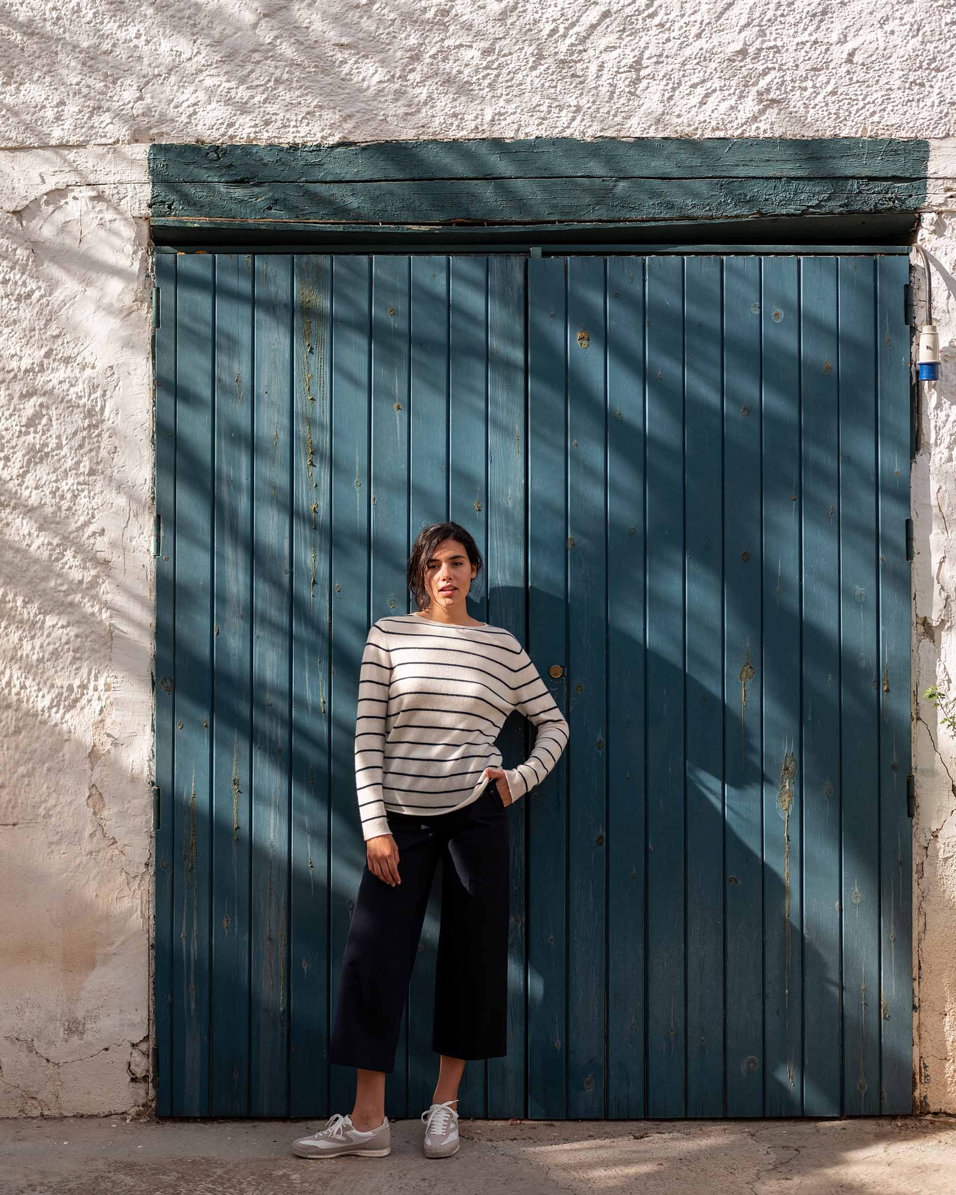 woman wearing Mersea carmel cashmere sweater in navy stripes standing in front of wooden door