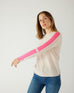 woman wearing mersea carmel cashmere sweater in champagne color with hot pink stripes down sleaves with arm out