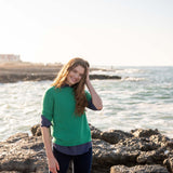 woman wearing mersea carmel sweater in jade standing near water on rocks