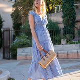 Woman in a blue striped dress holding a straw bag outdoors.