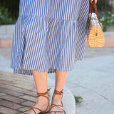 Person wearing a blue and white striped dress with brown sandals and a straw bag.