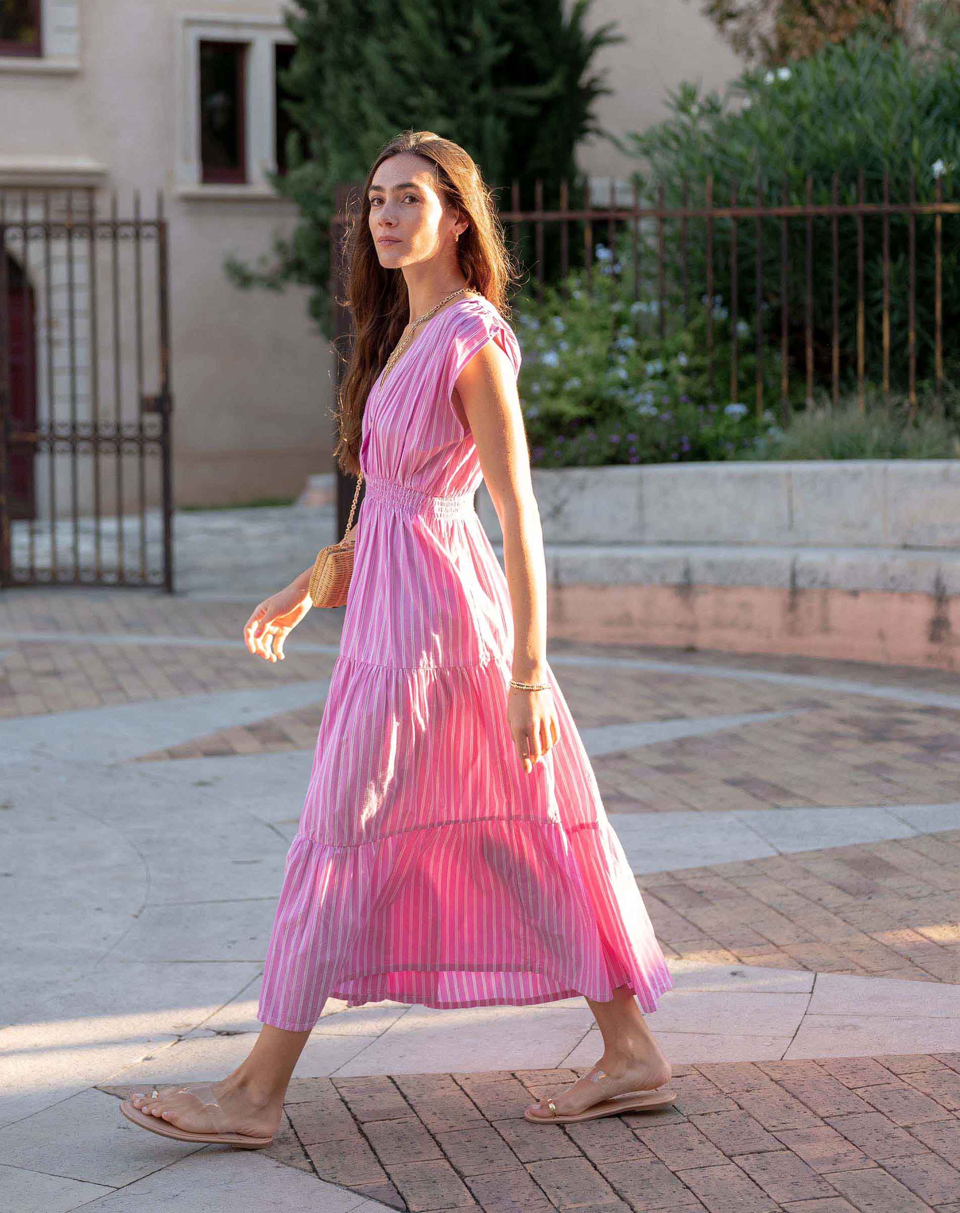 Woman in a pink dress walking outdoors on a sunny day.