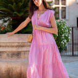 Woman in a pink dress standing outdoors with plants and a building in the background