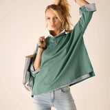 Woman wearing a green oversized shirt and light blue jeans against a beige background