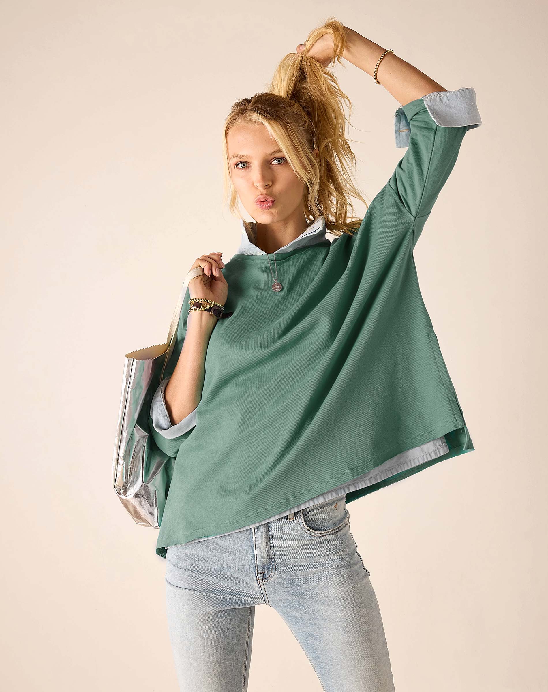 Woman wearing a green oversized shirt and light blue jeans against a beige background