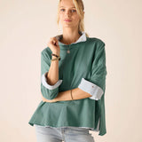 Woman wearing a green sweater with rolled-up sleeves against a beige background