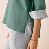 Person wearing a green shirt with rolled-up sleeves and light gray pants on a beige background