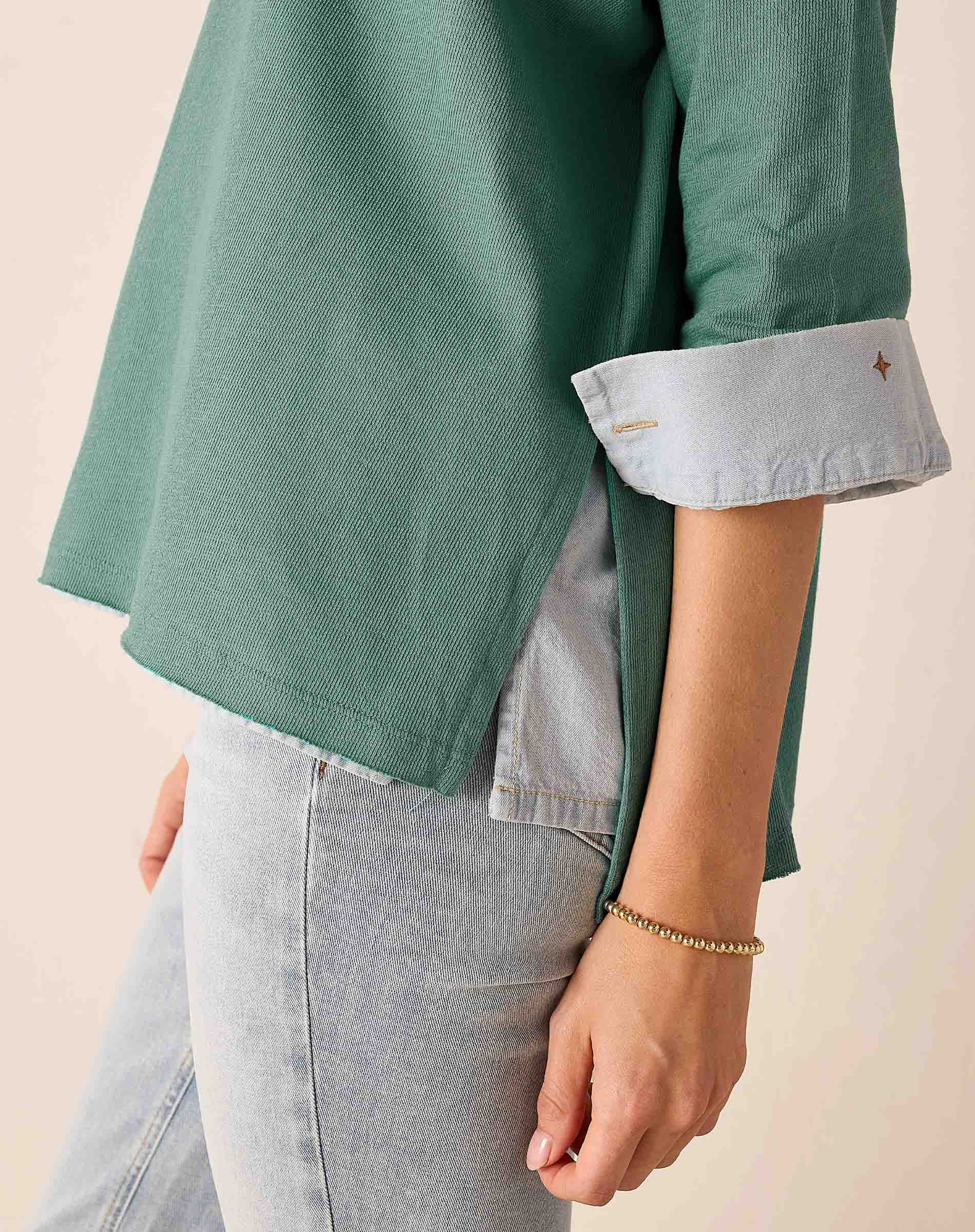 Person wearing a green shirt with rolled-up sleeves and light gray pants on a beige background