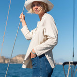 Woman on a sailboat wearing a white hat and light jacket with a blue sea and sky background