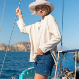 Woman on a boat wearing a white shirt and blue shorts with a scenic background