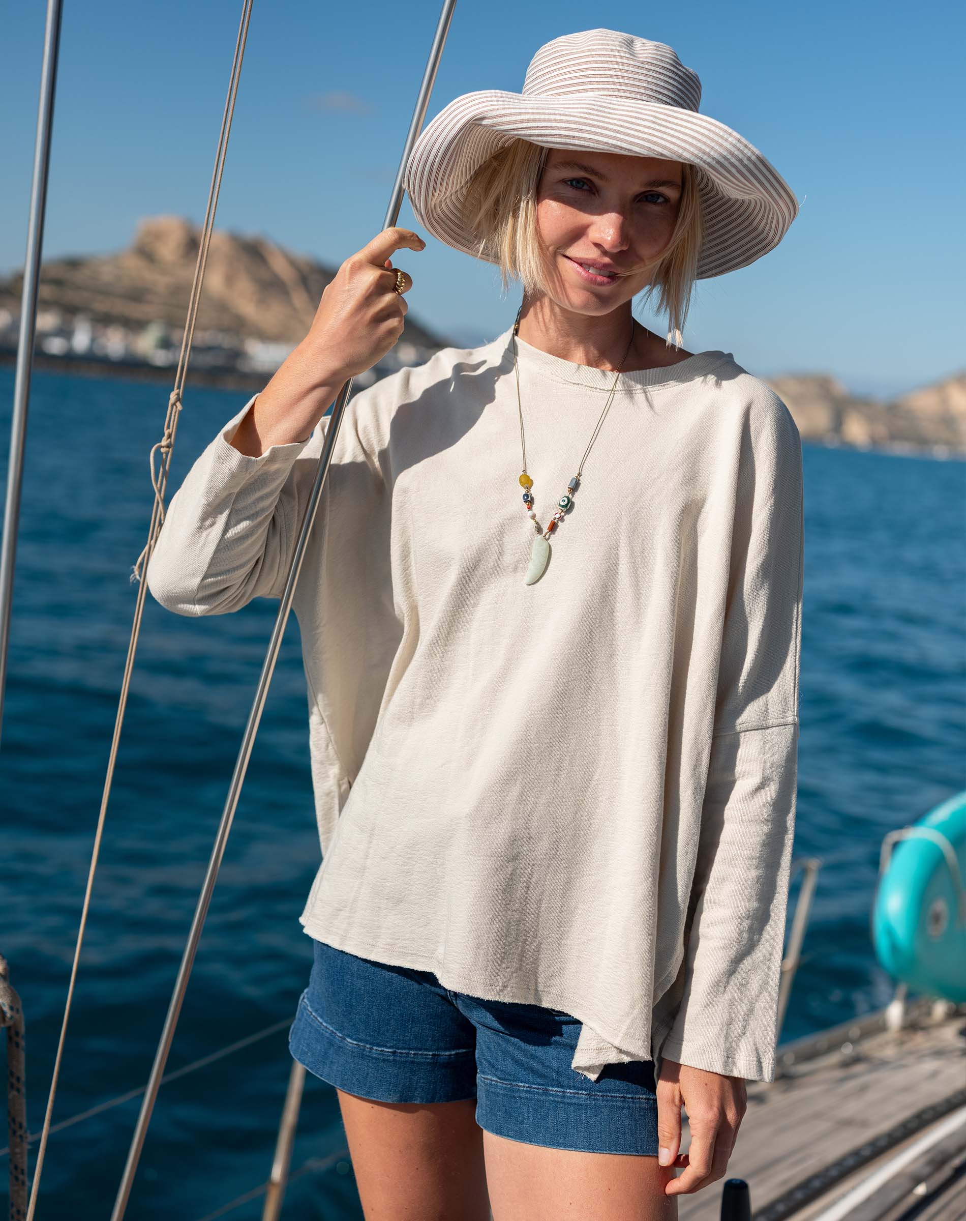 Woman on a boat wearing a wide-brimmed hat and casual outfit with a scenic background.