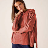 Woman wearing a rust-colored sweater and dark pants against a plain background