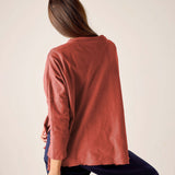 Person wearing a rust-colored long-sleeve top and dark pants on a plain background