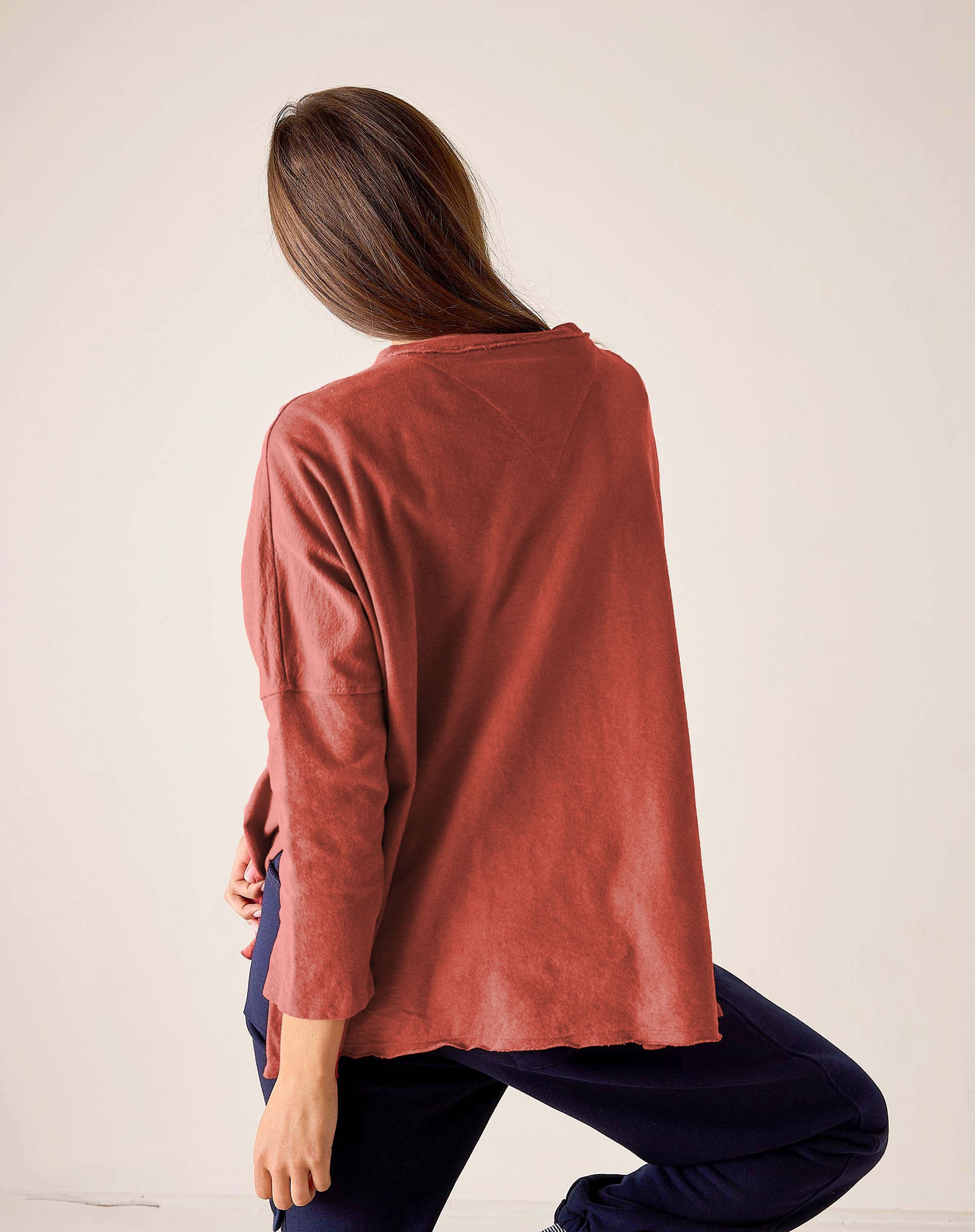 Person wearing a rust-colored long-sleeve top and dark pants on a plain background