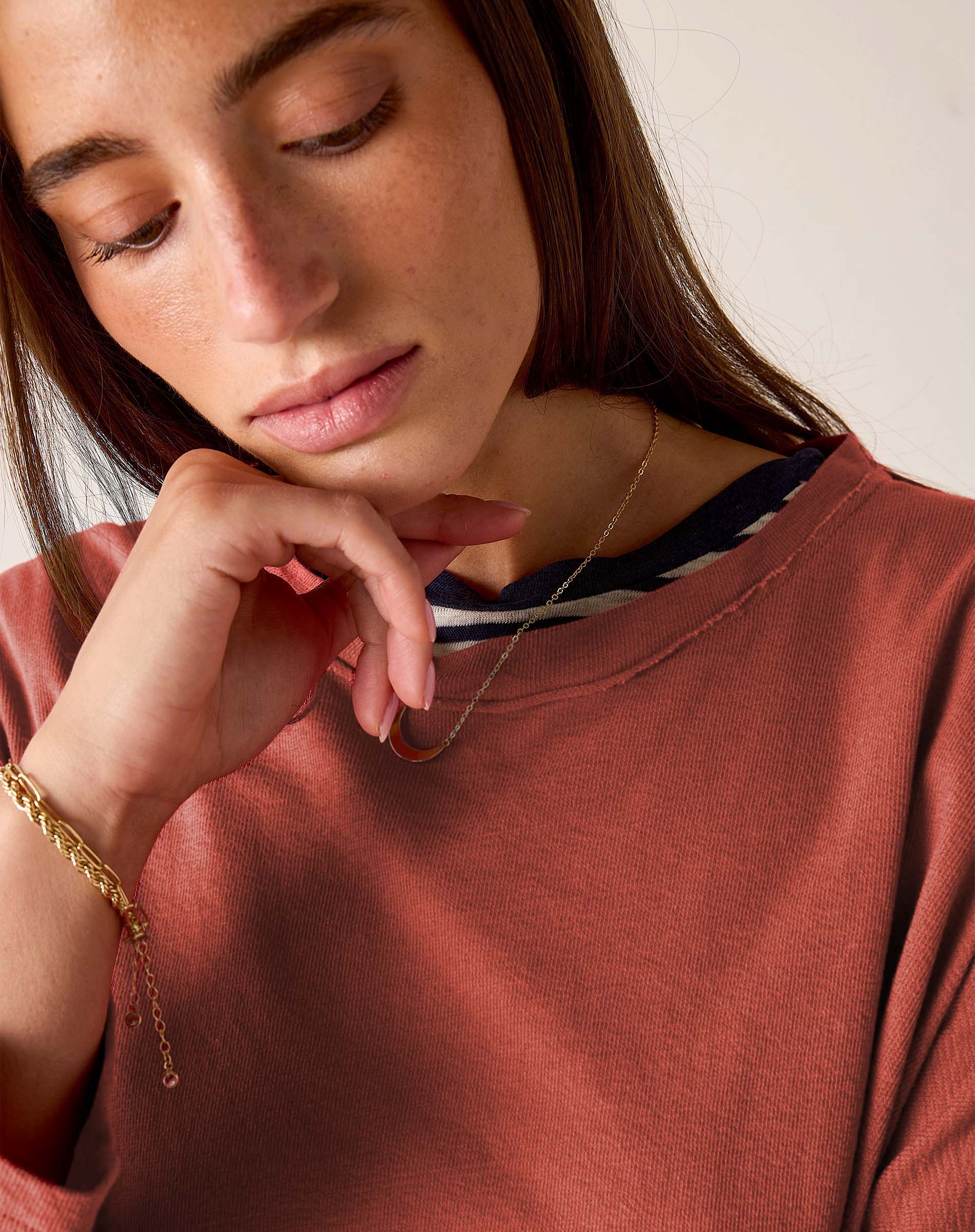 Woman wearing a gold necklace and bracelet, with a neutral background