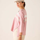 Woman wearing a pink long-sleeve shirt with white stripes and a beige cap on a plain background