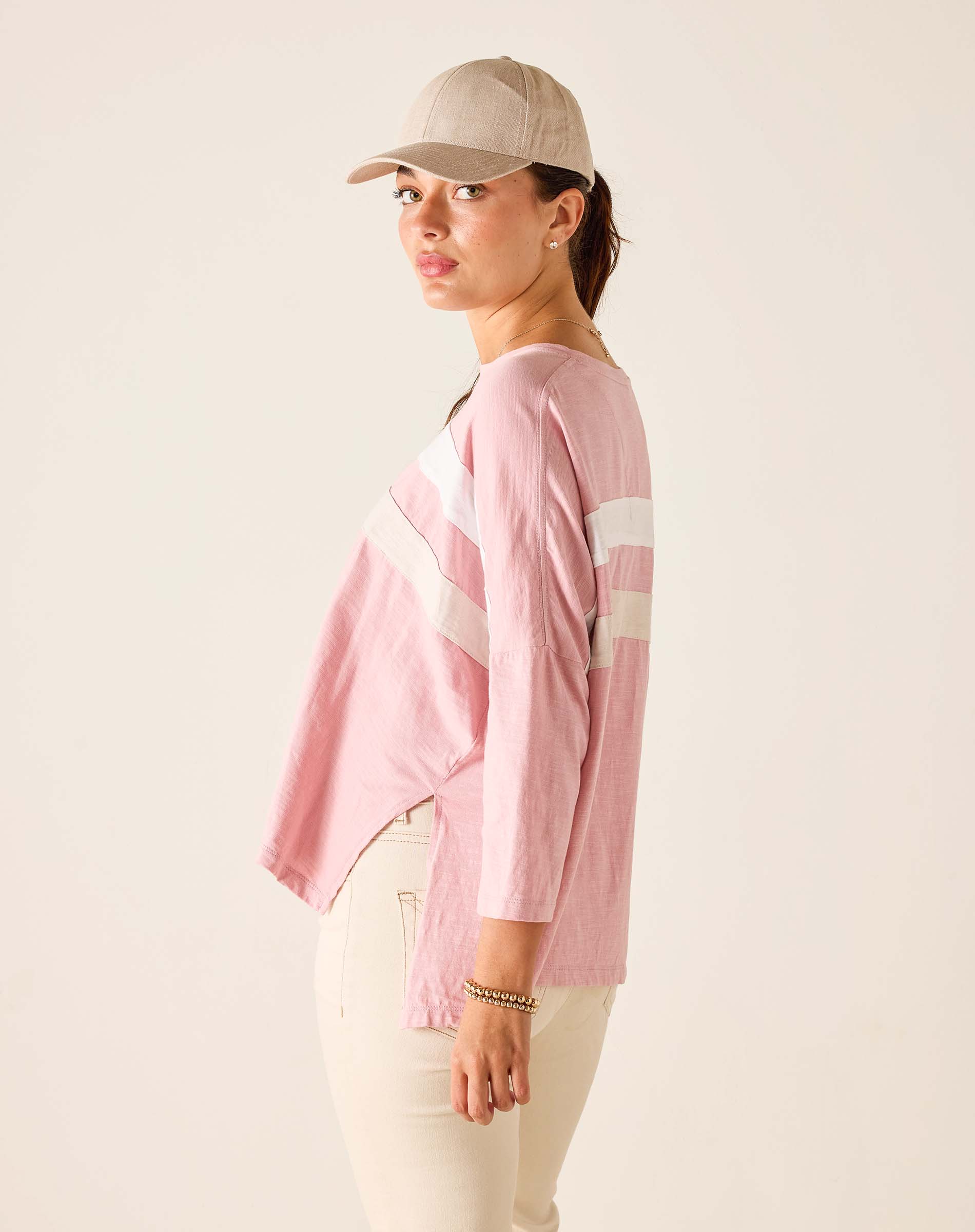 Woman wearing a pink long-sleeve shirt with white stripes and a beige cap on a plain background