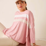 Person wearing a pink long-sleeve top with white stripes and a beige cap, sitting on a beige couch.