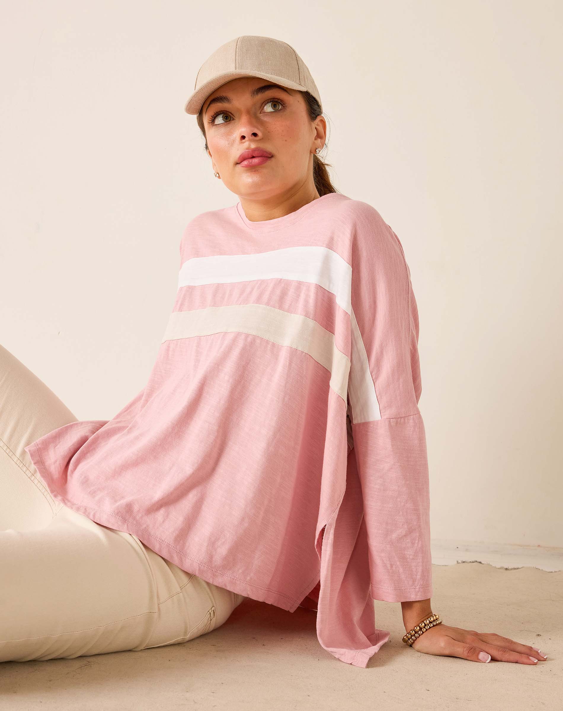 Person wearing a pink long-sleeve top with white stripes and a beige cap, sitting on a beige couch.