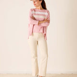 Woman wearing a pink striped sweater, beige pants, and a cap against a plain background