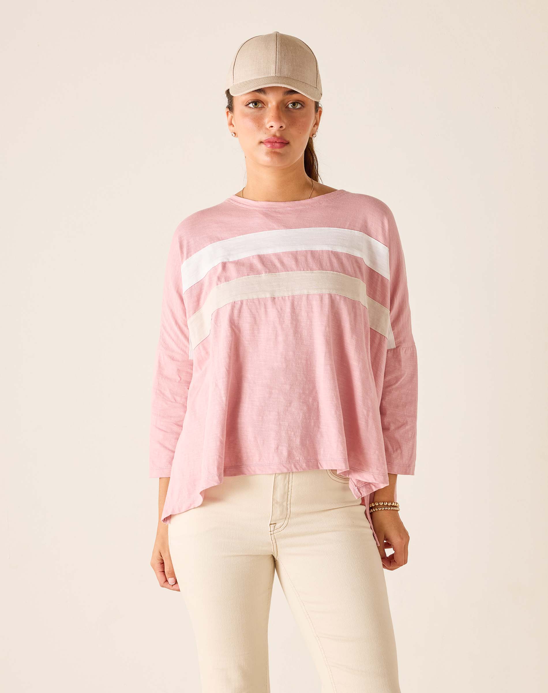 Woman wearing a pink long-sleeve top with white stripes and a beige cap on a plain background