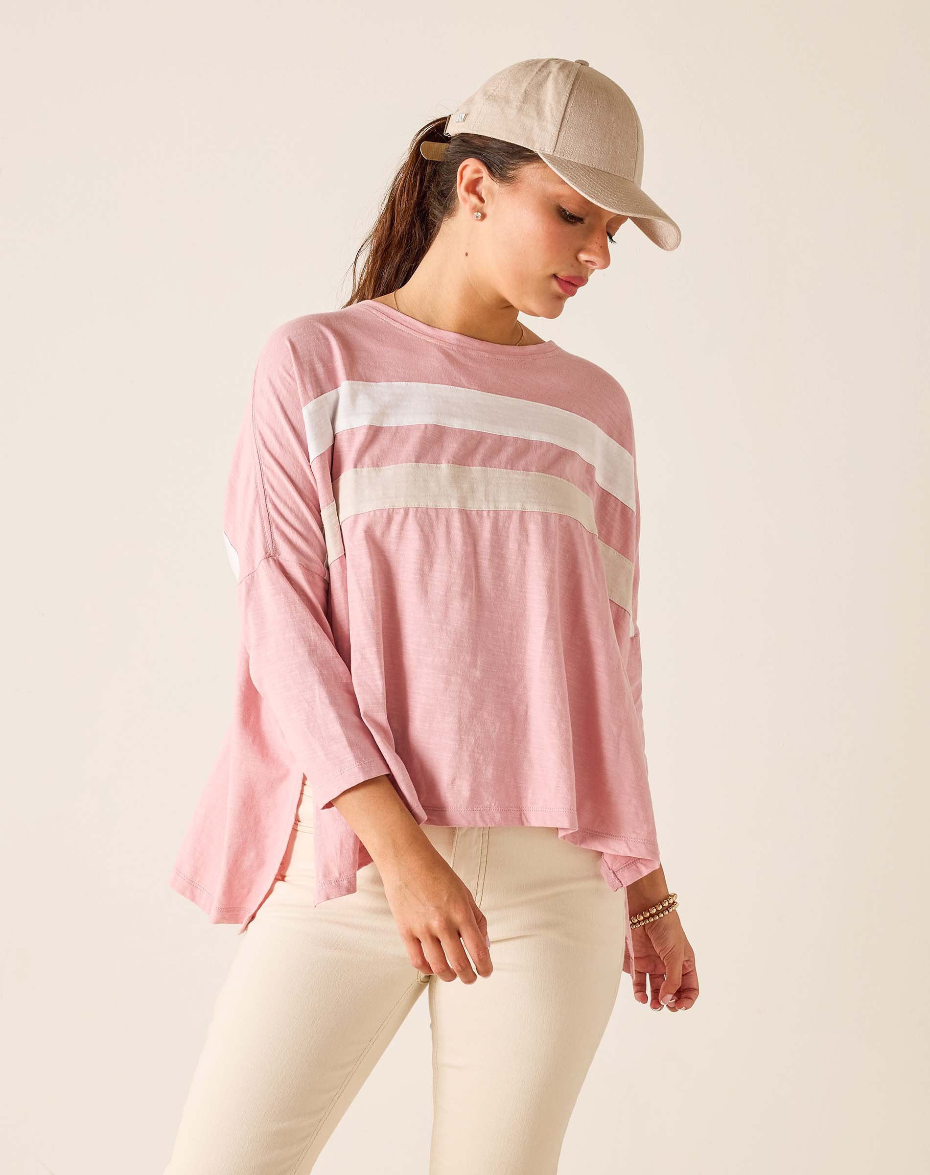 Woman wearing a pink striped shirt and beige cap on a plain background