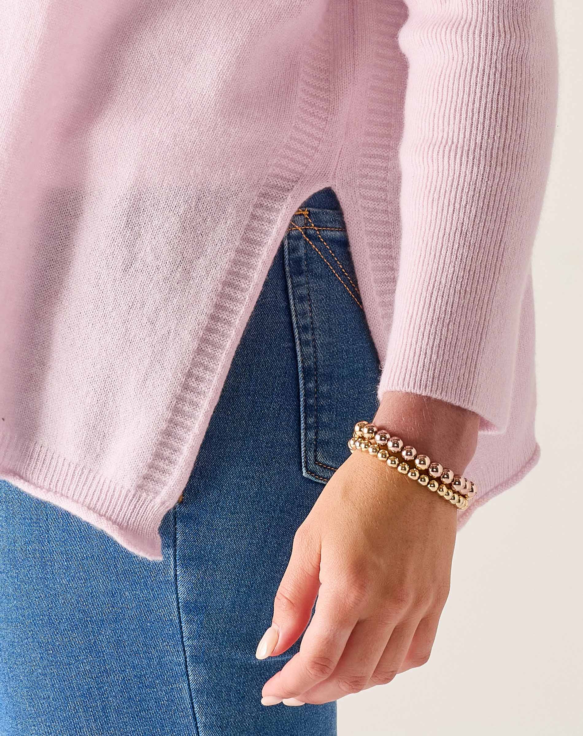 Person wearing a pink sweater and blue jeans with a gold bracelet on a light background
