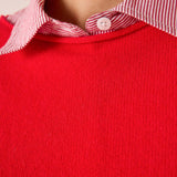 Scarlet red cashmere knit sweater layered over a pink and white striped button-down shirt.