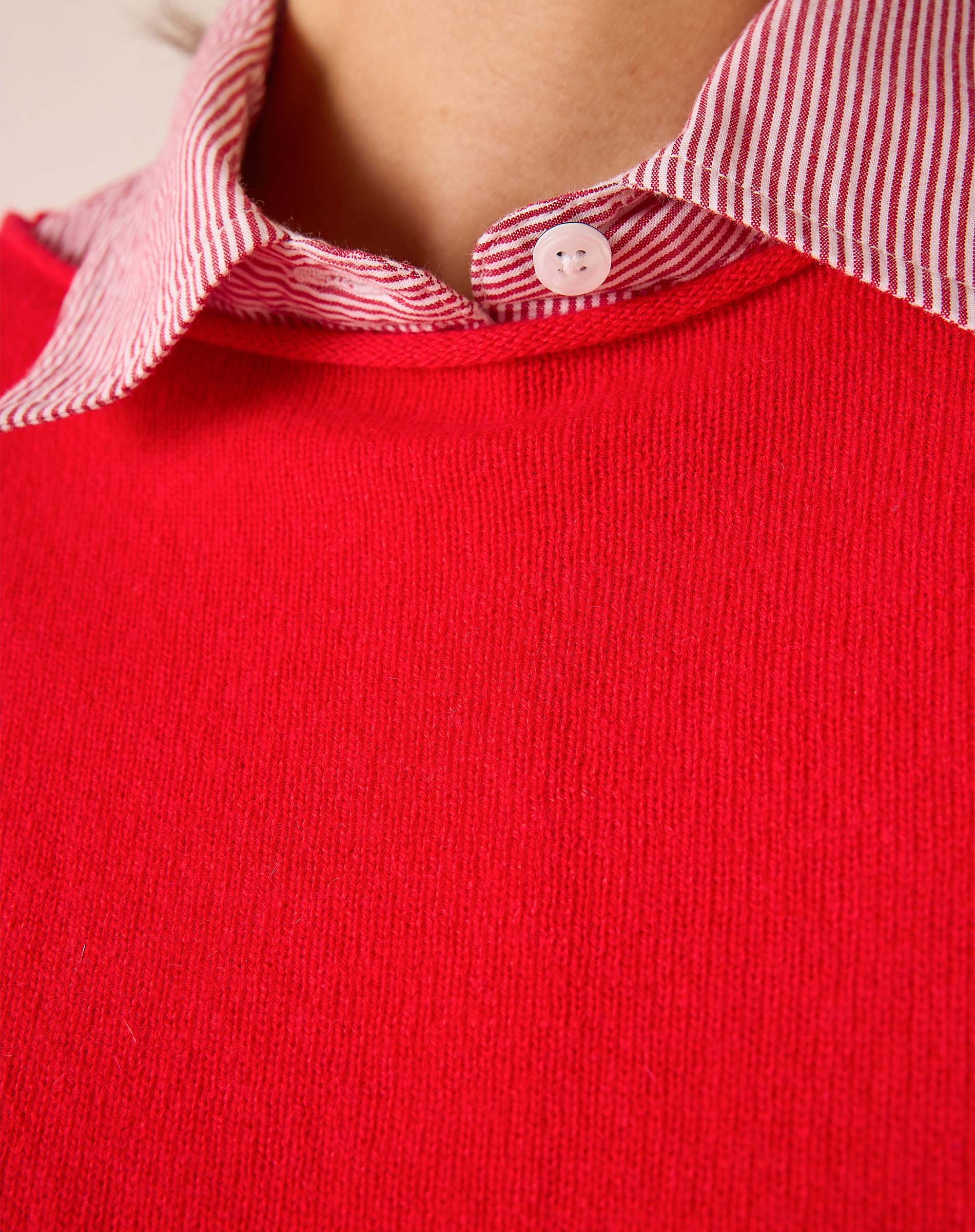 Scarlet red cashmere knit sweater layered over a pink and white striped button-down shirt.