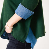 Hunter green ribbed cashmere sweater with rolled denim cuffs and a gold bead bracelet.