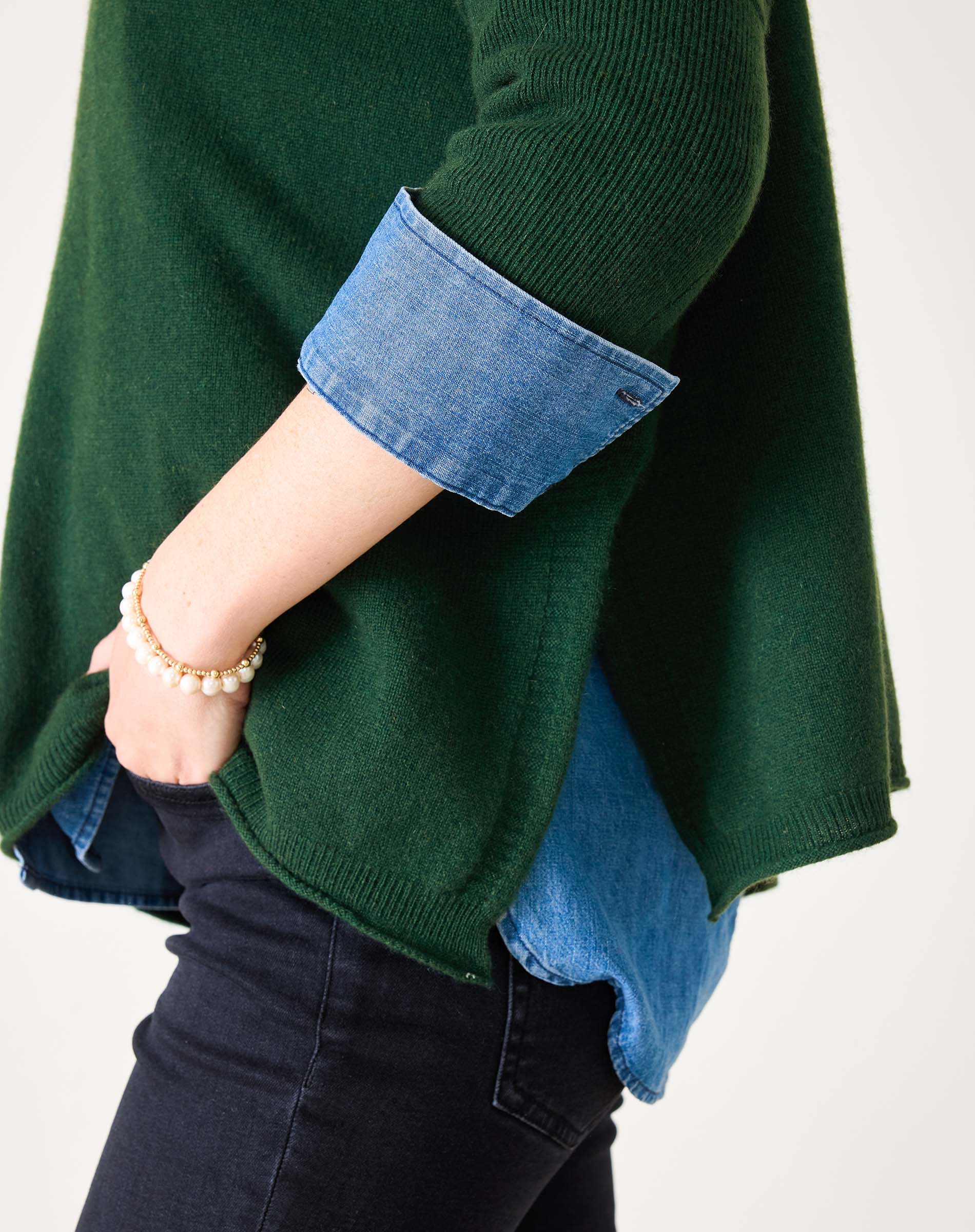 Hunter green ribbed cashmere sweater with rolled denim cuffs and a gold bead bracelet.