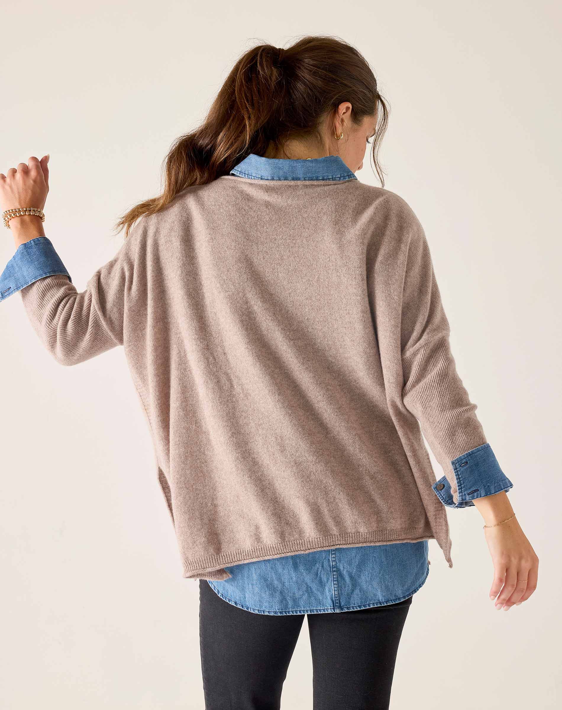 Back view of women's travel-friendly toast colored cashmere sweater with relaxed fit and layered denim shirt.
