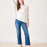 Woman wearing a white sweater, blue jeans, and yellow sneakers on a plain background