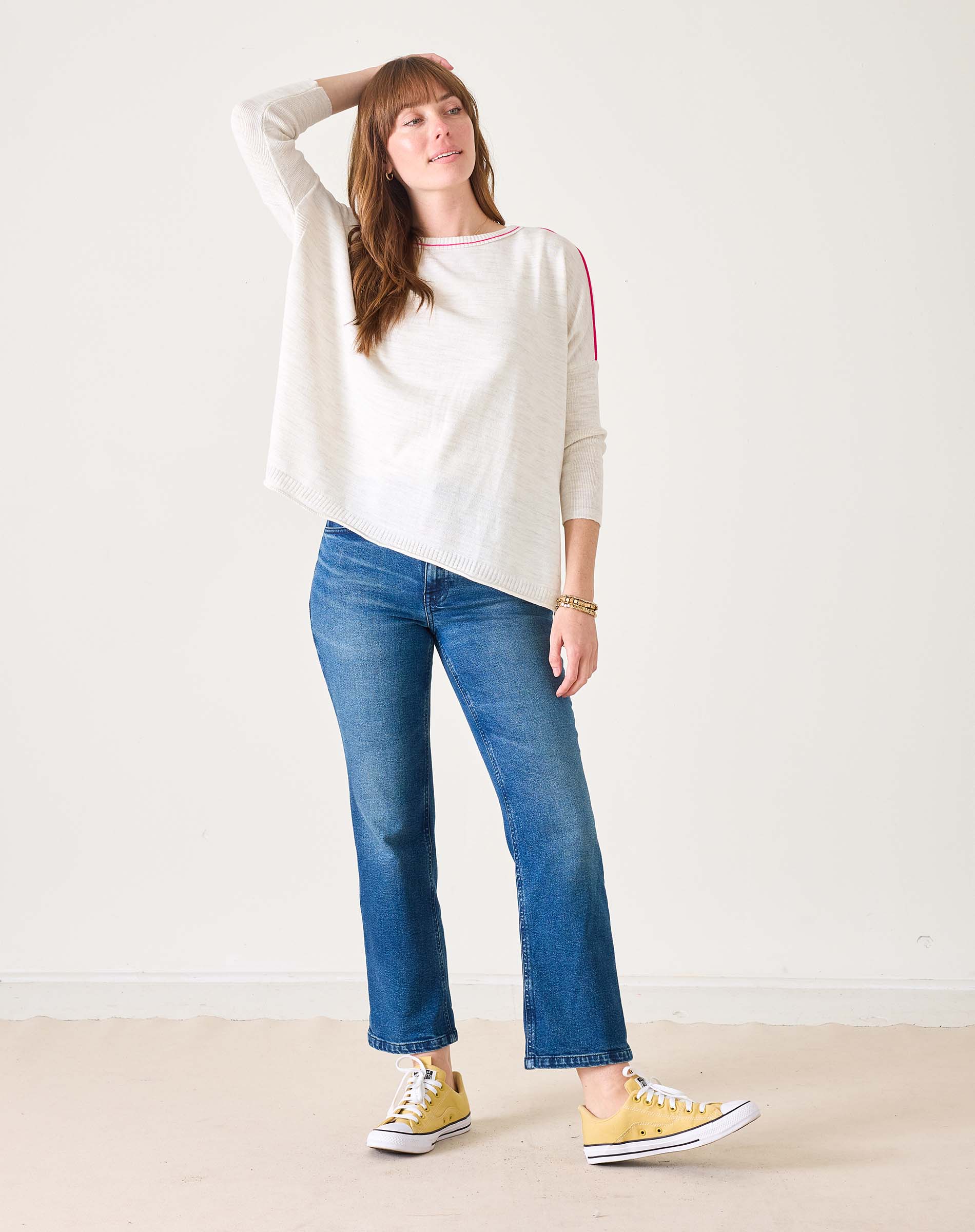 Woman wearing a white sweater, blue jeans, and yellow sneakers on a plain background