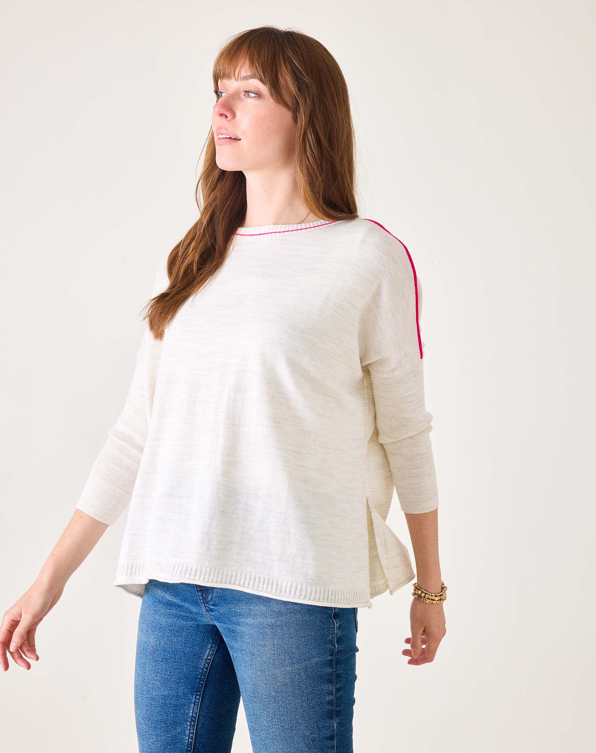 Woman wearing a cream sweater with red accents and blue jeans on a white background