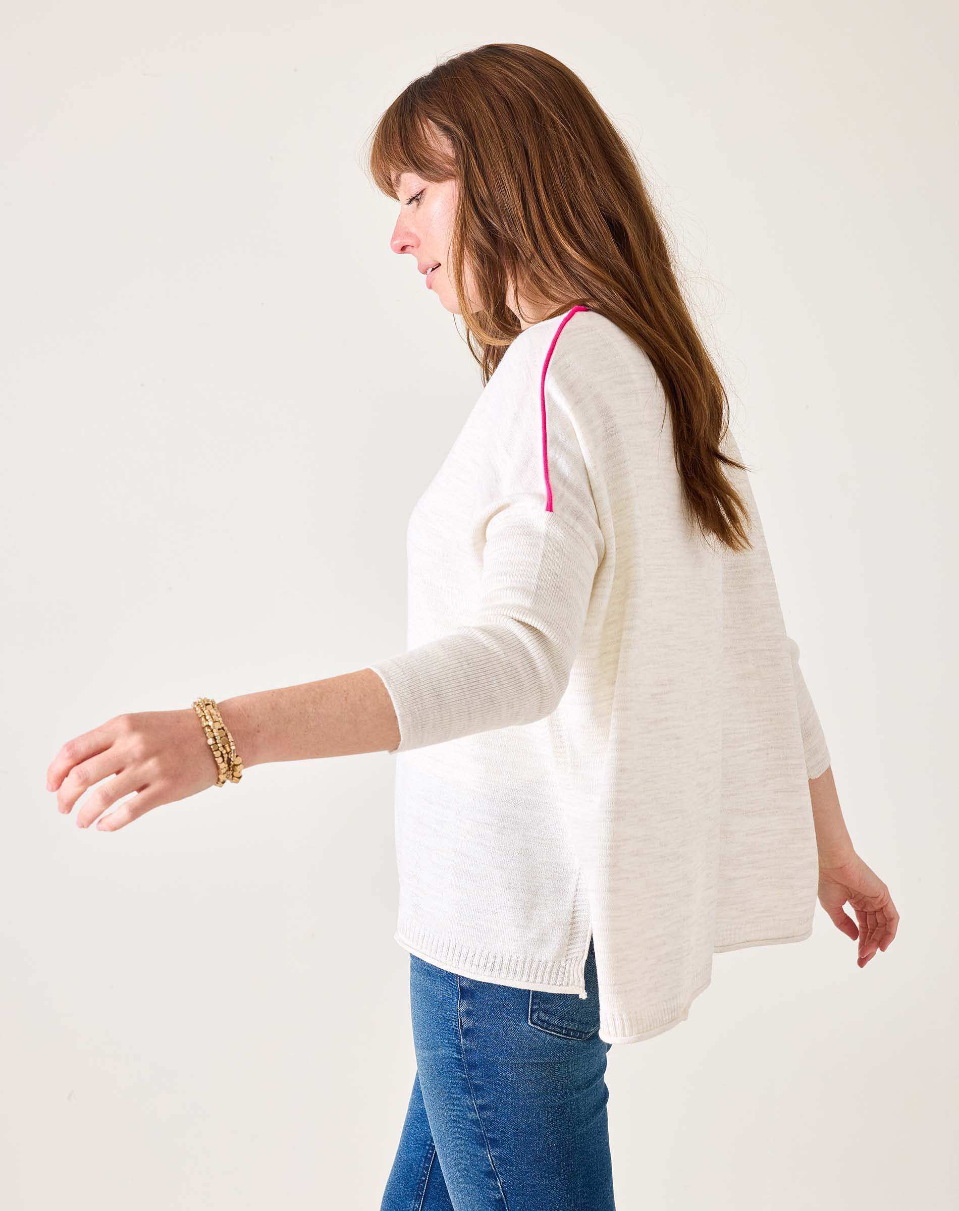 Woman wearing a white cardigan and blue jeans on a plain background