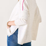 Person wearing a white sweater with pink trim and blue jeans on a plain background
