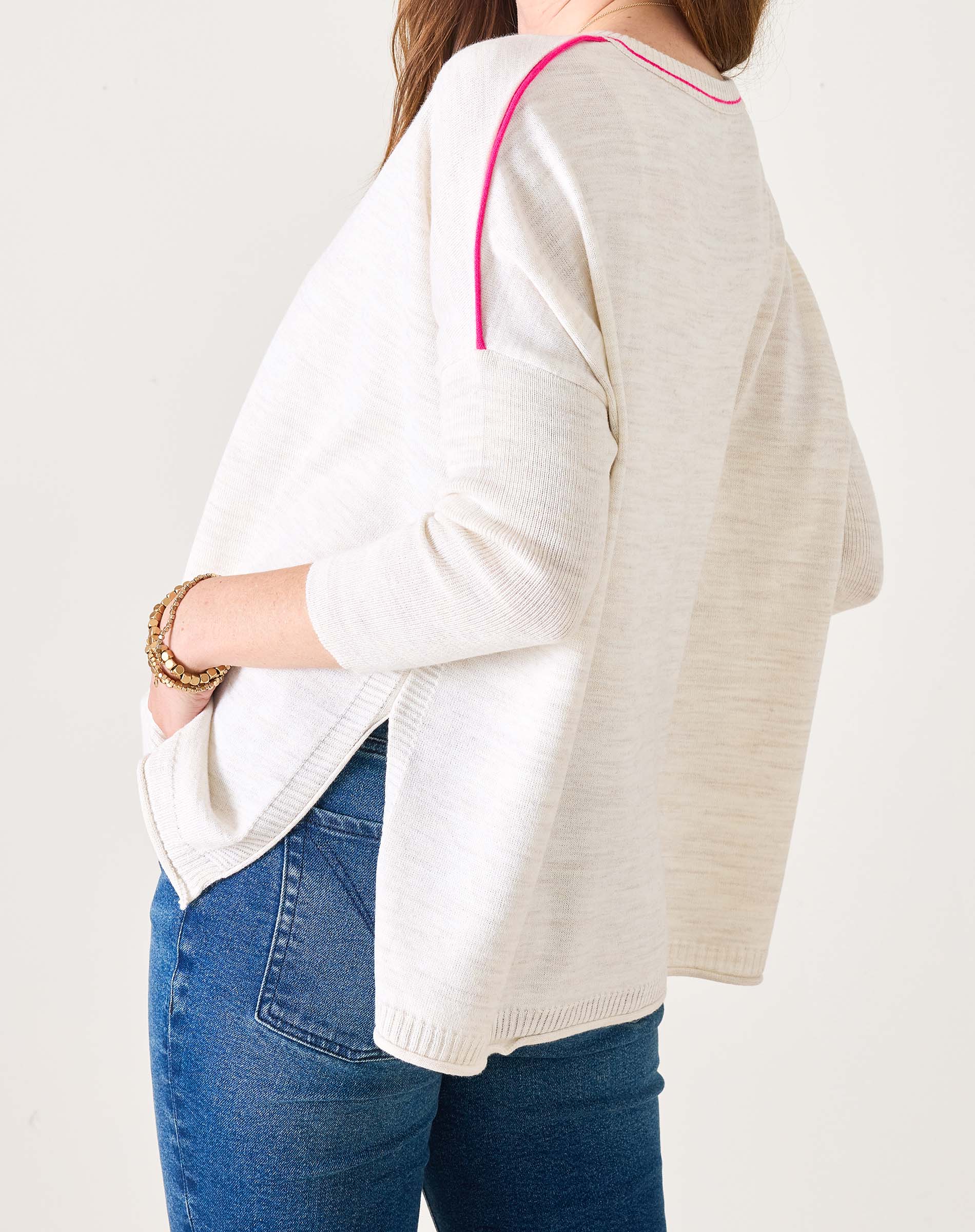 Person wearing a white sweater with pink trim and blue jeans on a plain background