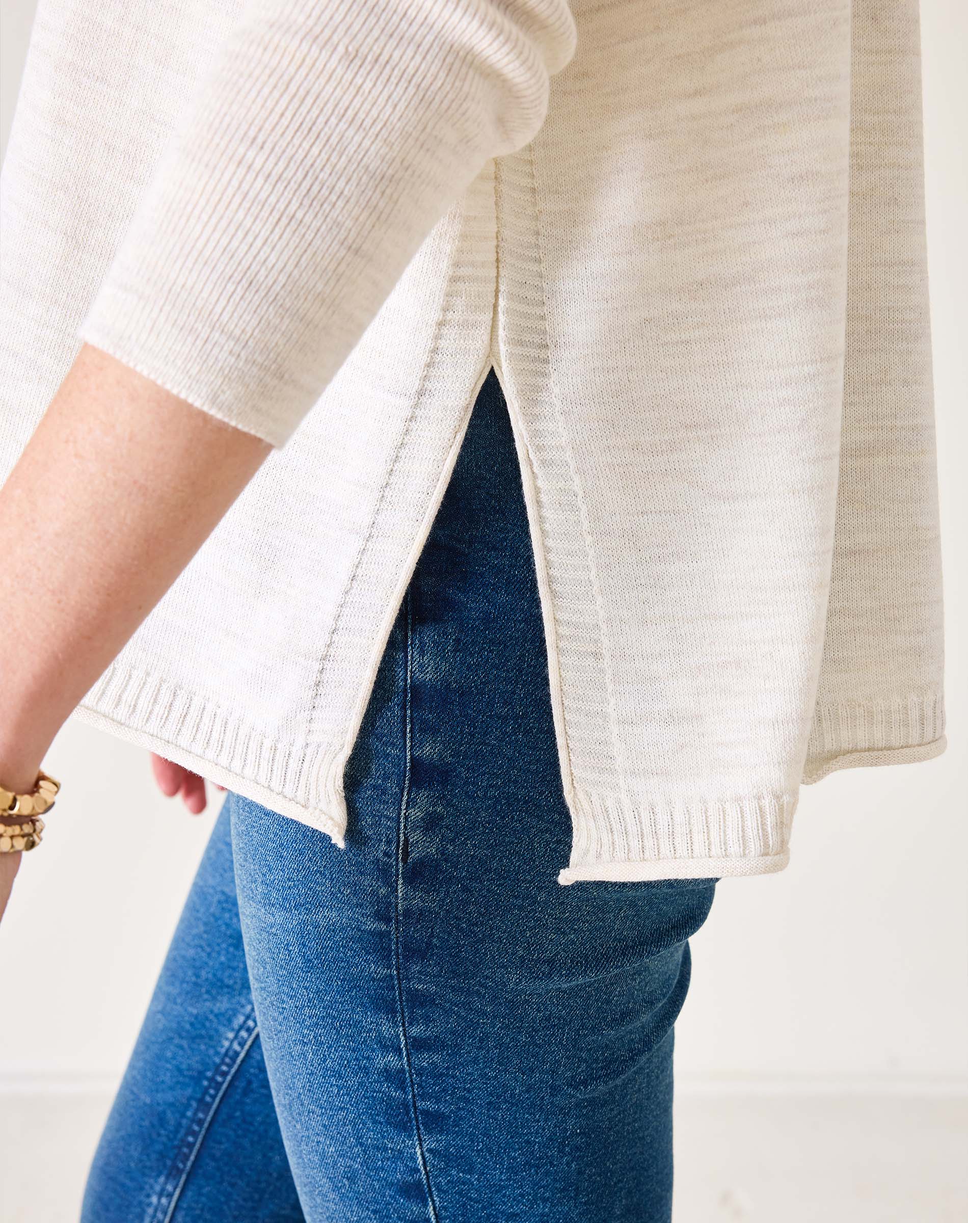 Person wearing a white sweater and blue jeans on a plain background