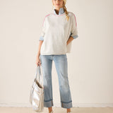 Woman wearing a light-colored sweater with rolled-up sleeves and light blue jeans, holding a silver tote bag.