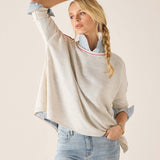 Woman wearing a beige sweater with rolled-up sleeves and light blue jeans against a plain background