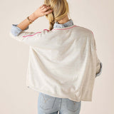 Person wearing a light-colored poncho over a denim shirt and jeans on a beige background