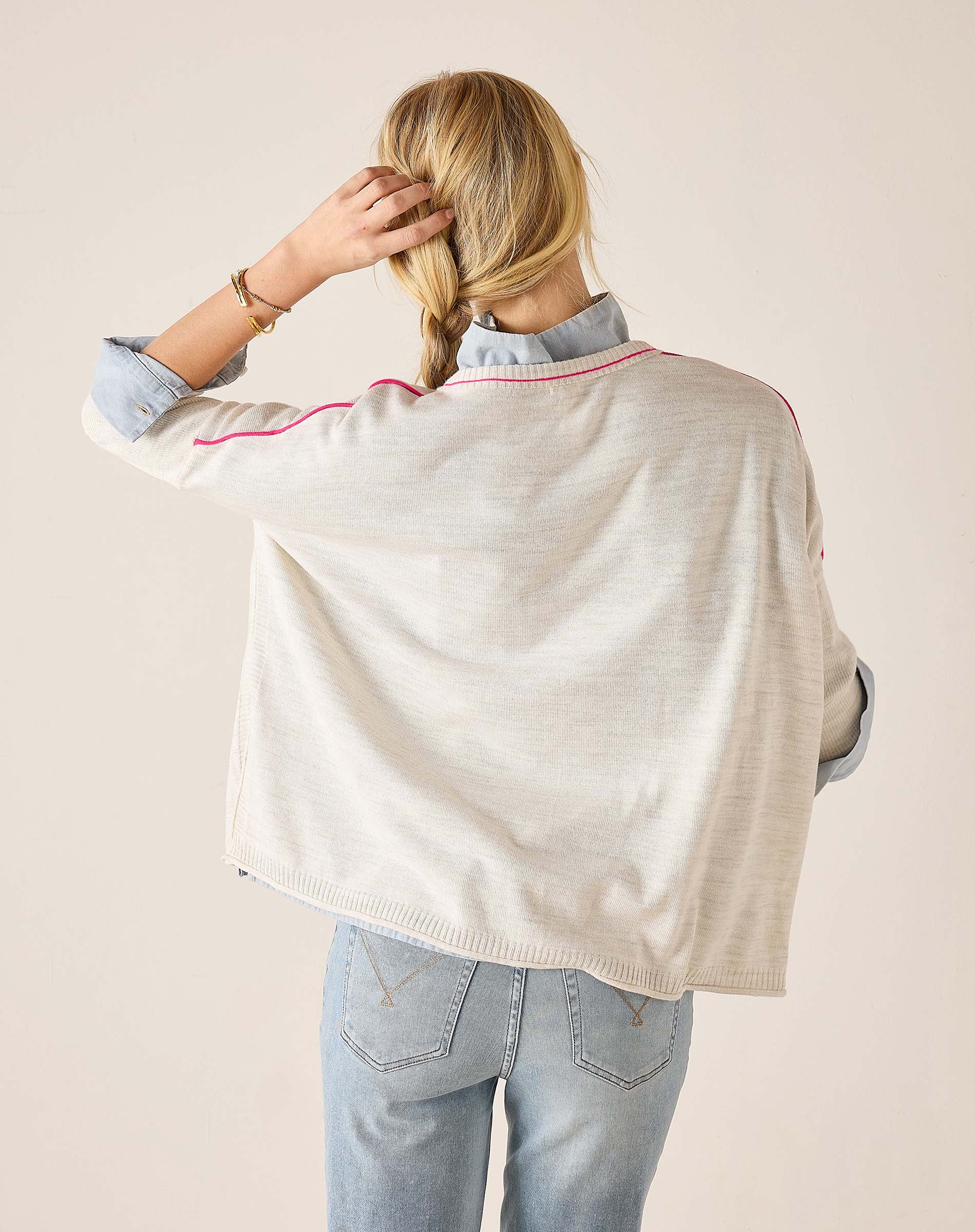 Person wearing a light-colored poncho over a denim shirt and jeans on a beige background