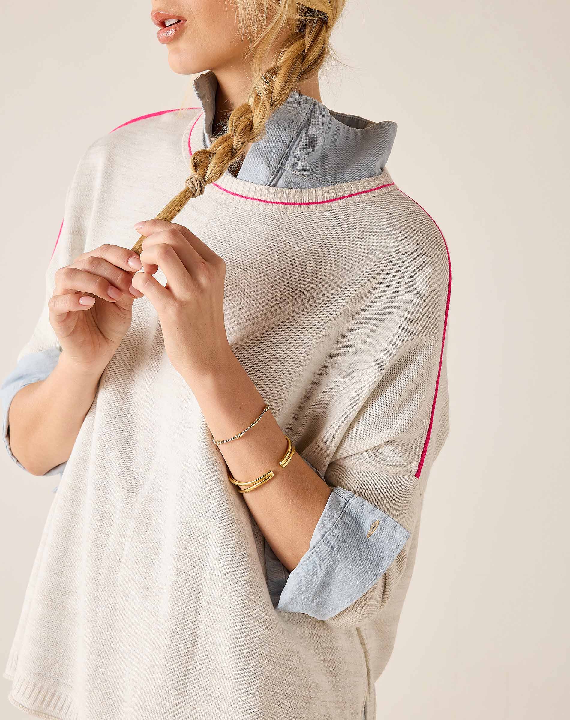 Woman wearing a light gray sweater with rolled-up sleeves and a braid, on a plain background