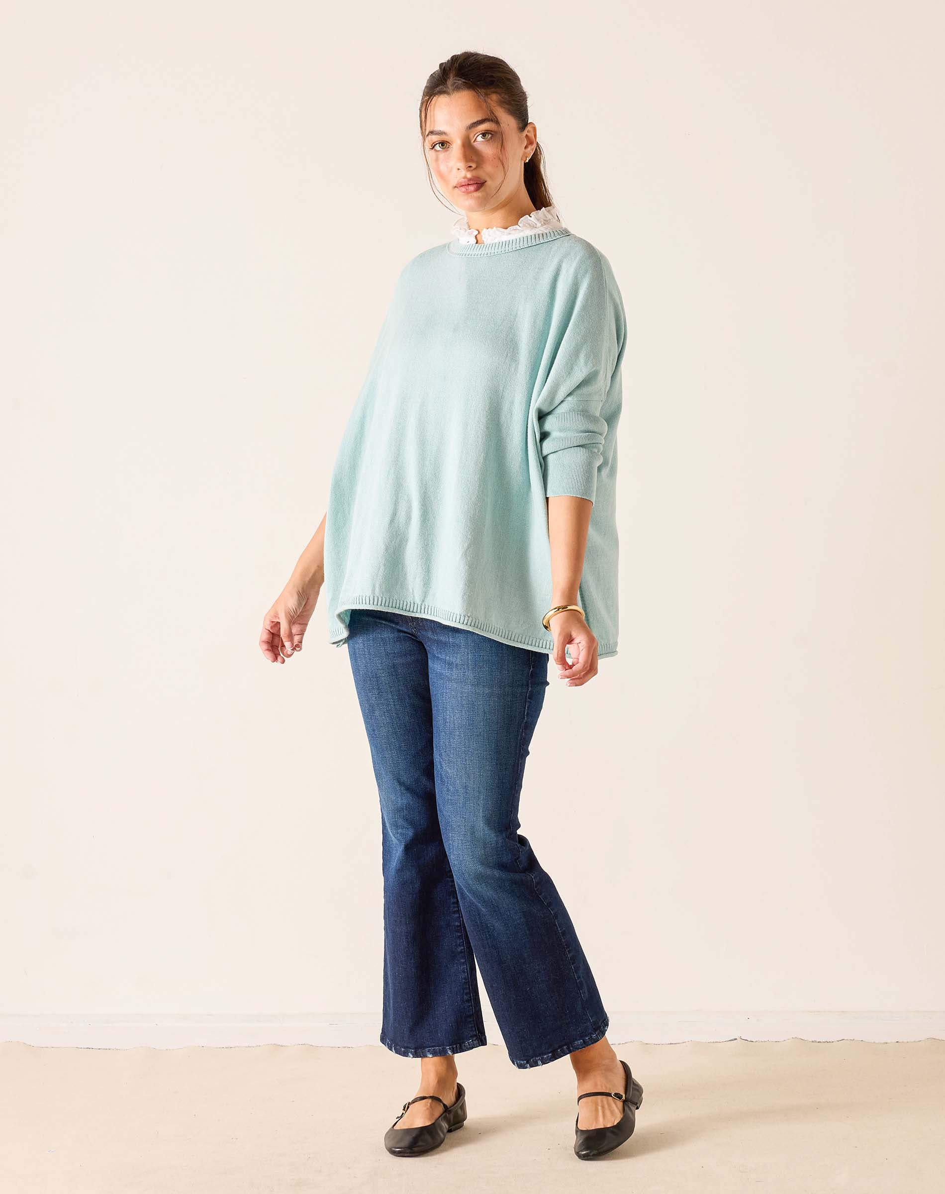 Woman wearing a light blue sweater and dark blue jeans against a white background
