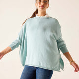 Woman wearing a light blue sweater and blue jeans against a plain background