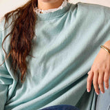Person wearing a light blue sweater with a white collar, sitting on a blue cushion.