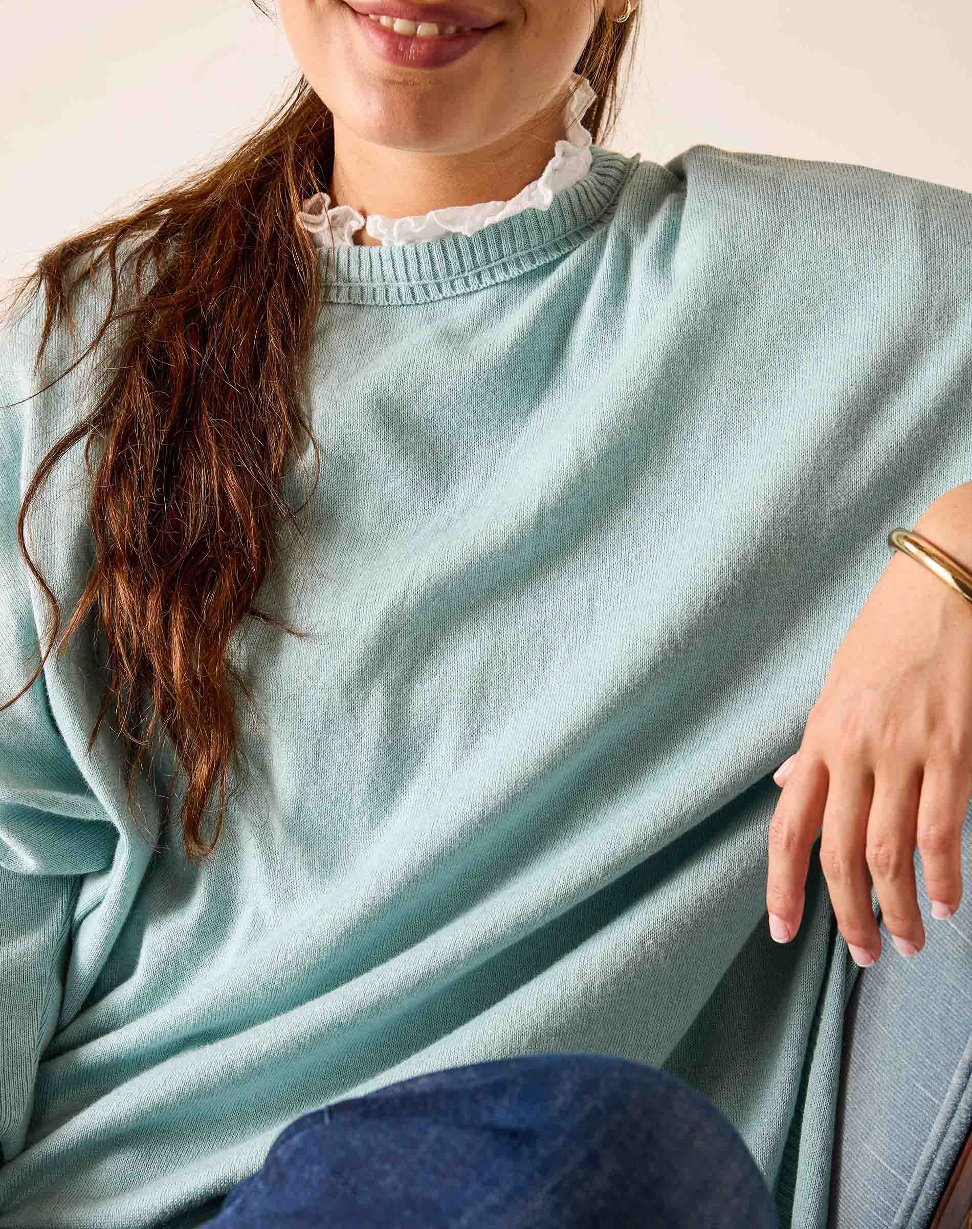 Person wearing a light blue sweater with a white collar, sitting on a blue cushion.